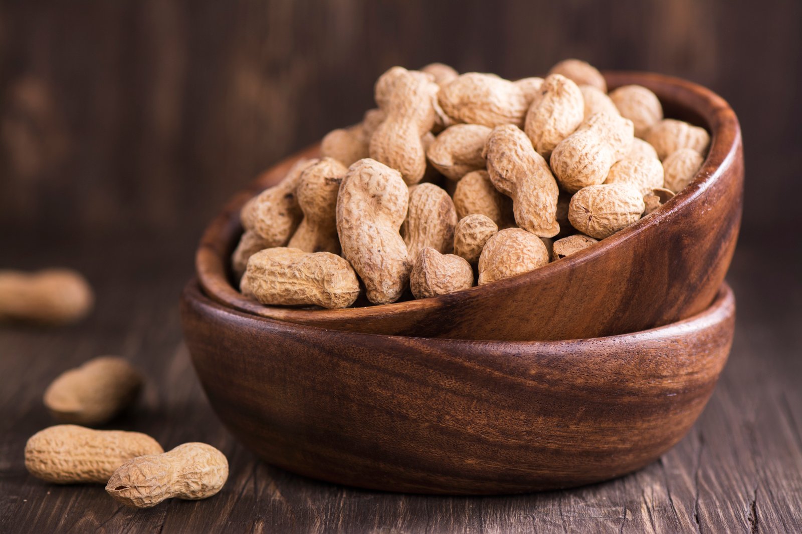 Raw peanuts in wooden bowls over grunge wooden background. Selective focus