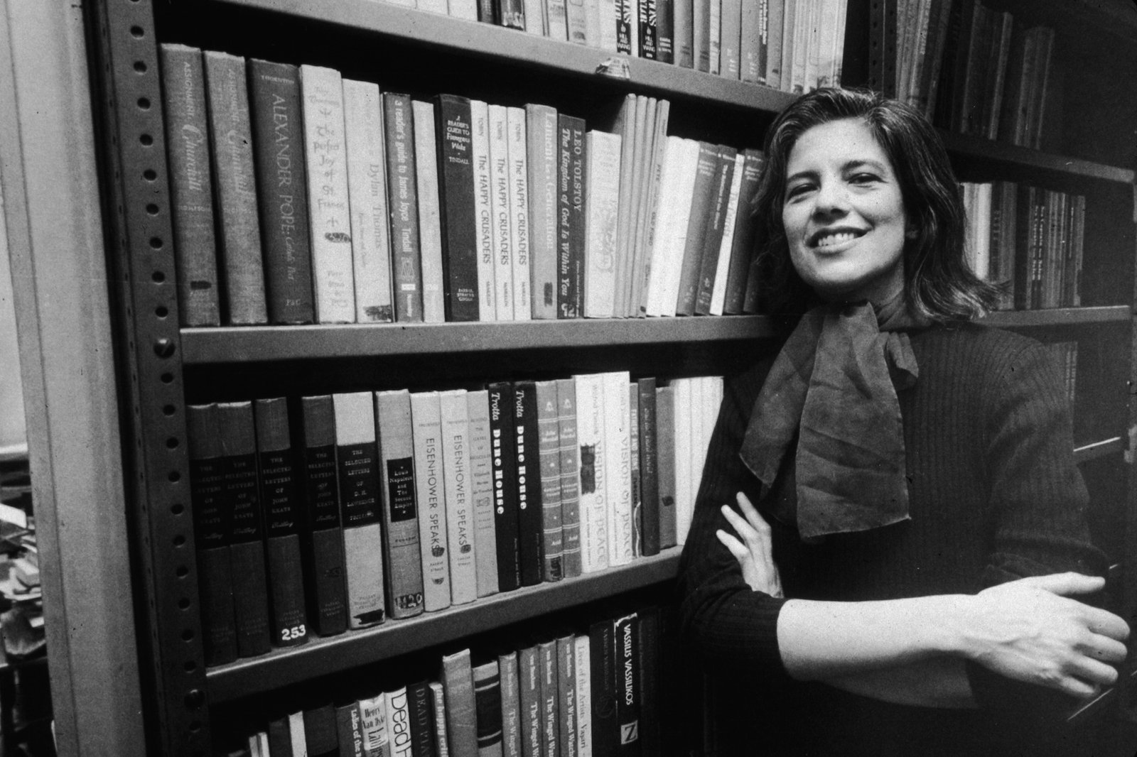 Portrait of American author and critic Susan Sontag (1933 - 2004) smiles broadly as she leans, arms crossed, against a bookshelf in the offices of her publisher, Farrar, Straus, and Giroux, New York, New York, January 23, 1978. (Photo by William E. Sauro/New York Times Co./Getty Images)